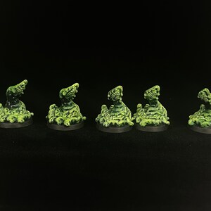 May include: Five miniature fantasy figures, each with a green and black color scheme. The figures appear to be monsters or creatures, possibly for tabletop gaming or collecting. They are set against a black background.
