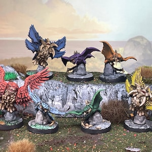 Puede incluir: Una colección de figuras en miniatura de fantasía, cada una representando una criatura alada con detalles intrincados. Las figuras están pintadas en varios colores, incluyendo rojo, azul, morado y amarillo, y están montadas sobre pequeñas bases redondas.