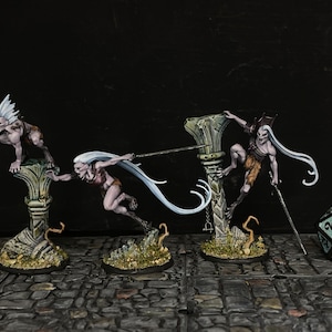 May include: Miniature fantasy figures of pale-skinned creatures with long white hair, posed on decorative columns. One figure is climbing, another is lunging with a weapon, and a third is perched. A twenty-sided die is in the foreground.