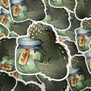 May include: A green dinosaur with spikes on its back is holding a jar of pickles. The jar has a label that says "Pickles".