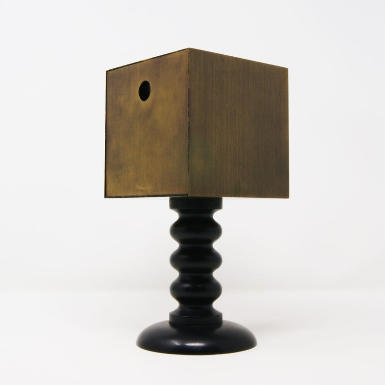 May include: A wooden box with a round hole in the front, sitting on a black pedestal with a fluted base.