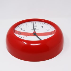 May include: A red, round clock with white face and black numbers. The clock has a red stripe across the face and the brand name "LORENZ" is printed on the face.