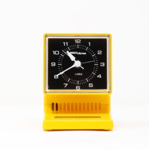 May include: A yellow plastic alarm clock with a black face and white hands. The clock face reads "MULTIchron" and "4 JEWELS".