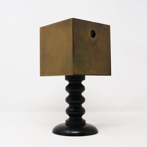 May include: A small, square, wooden box with a hole in the top, sitting on a black, turned wooden pedestal.