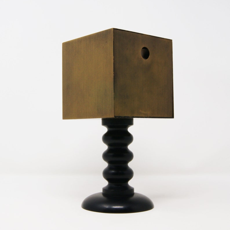 May include: A small, square, wooden box with a hole in the top, sitting on a black, turned wooden pedestal.