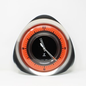 May include: A silver and orange analog clock with a black face and white hands. The clock is shaped like a teardrop and has a silver rim.