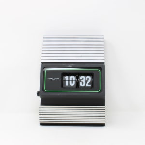 Könnte beinhalten: Eine schwarze Flip-Uhr mit grünem Rand und weißen Ziffern, die 10:32 anzeigen. Die Uhr hat einen silber-schwarz gestreiften Sockel und zeigt auf dem Zifferblatt "Tokyo Clock" an.