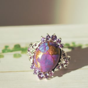 May include: A silver ring with a large oval purple and gold gemstone surrounded by smaller purple gemstones.