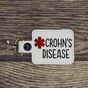 May include: White keychain with a red medical symbol and the text "CROHN'S DISEASE" in black.