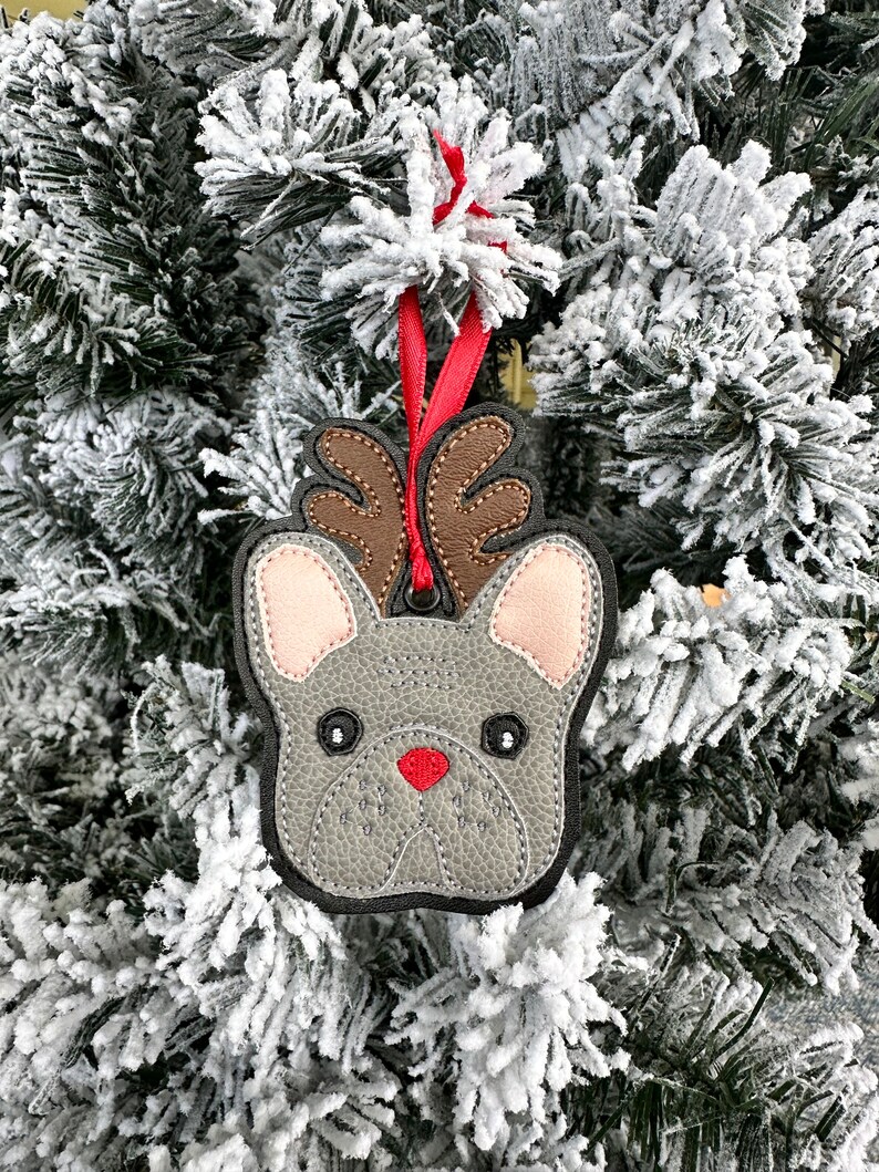 May include: A gray felt Christmas ornament shaped like a French bulldog with brown antlers and a red nose.