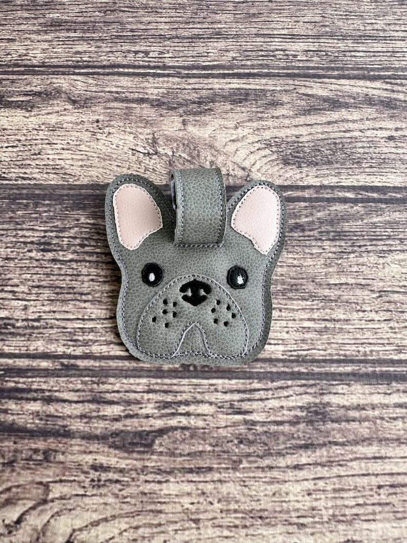 以下が含まれることがあります： ピンクの耳と黒い目をしたグレーの革製のフレンチブルドッグのキーホルダーです。
