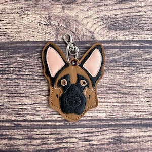 May include: A brown leather keychain with a black and pink German Shepherd dog face design.
