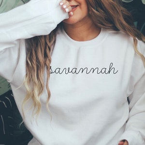 May include: White sweatshirt with the word "Savannah" written in black cursive script.