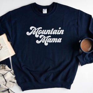 May include: A navy blue sweatshirt with the text "Mountain Mama" in white script lettering.
