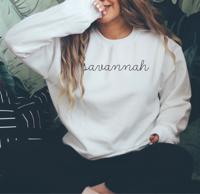 May include: White sweatshirt with the word "Savannah" written in black cursive script.