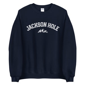 Peut inclure: Un sweat-shirt bleu marine avec le texte "JACKSON HOLE" en blanc et un graphique de montagne blanc.