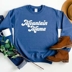 May include: A blue sweatshirt with the text "Mountain Mama" in white retro-style lettering.