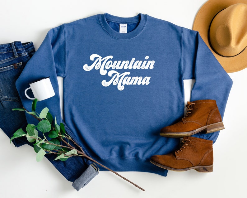 May include: A blue sweatshirt with the text "Mountain Mama" in white retro-style lettering.