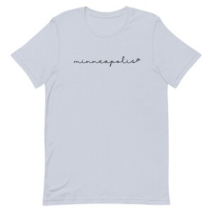 May include: Light blue t-shirt with the word "minneapolis" written in black cursive script.