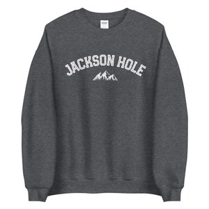 Peut inclure: Un sweat-shirt gris fonc&eacute; avec le texte "JACKSON HOLE" en blanc, avec un graphique de montagne blanc en dessous.