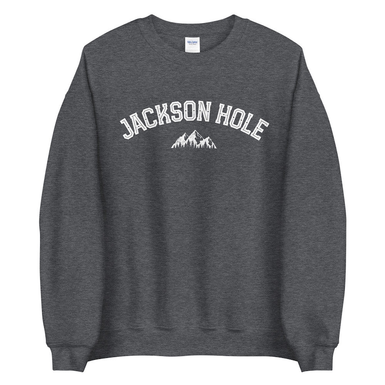 Peut inclure: Un sweat-shirt gris fonc&eacute; avec le texte "JACKSON HOLE" en blanc, avec un graphique de montagne blanc en dessous.
