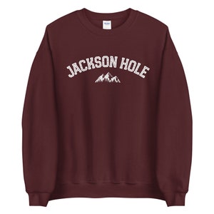 Peut inclure: Un sweat-shirt bordeaux avec le texte "JACKSON HOLE" en blanc et un motif de montagne.
