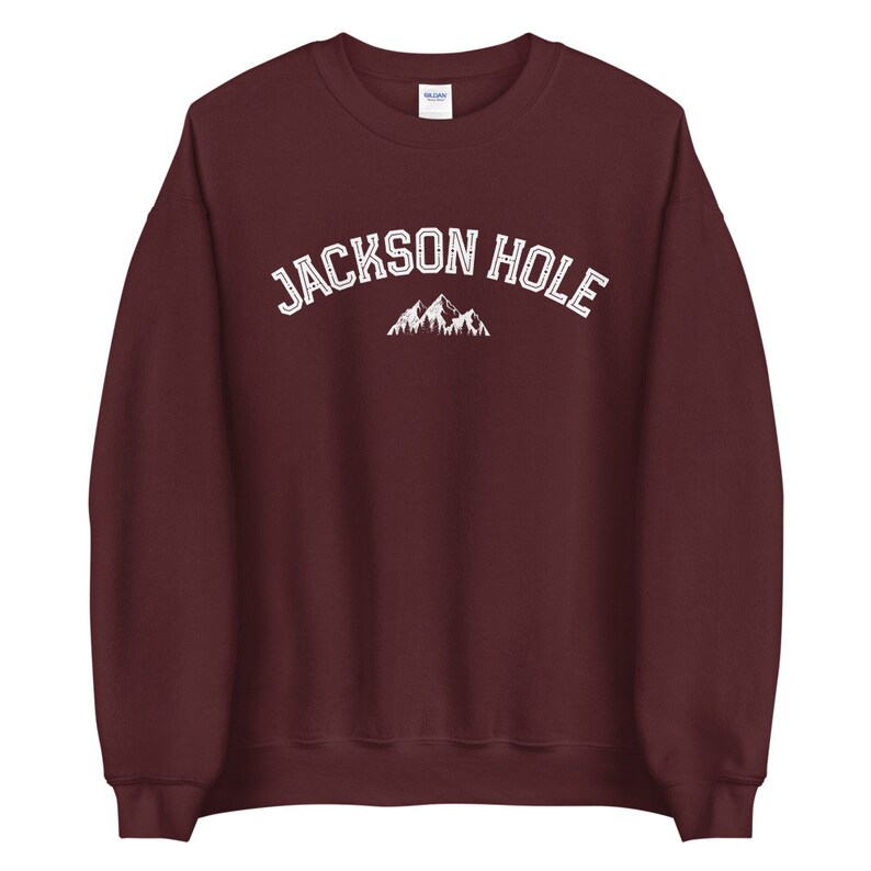 Peut inclure: Un sweat-shirt bordeaux avec le texte "JACKSON HOLE" en blanc et un motif de montagne.