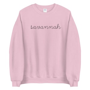 May include: A pink sweatshirt with the word "savannah" written in black cursive script.