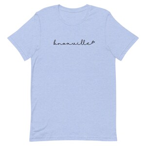 May include: Light blue t-shirt with the word "knoxville" in a cursive font. The word is in black and has a small heart at the end. The shirt is made of a soft material.