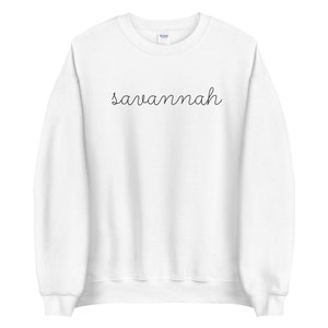 May include: White crewneck sweatshirt with the word "savannah" written in black cursive script.