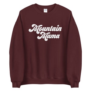 May include: A maroon sweatshirt with the text "Mountain Mama" in white retro-style lettering.