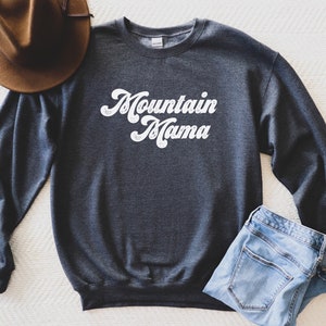May include: A dark grey sweatshirt with the text "Mountain Mama" in white retro-style lettering.