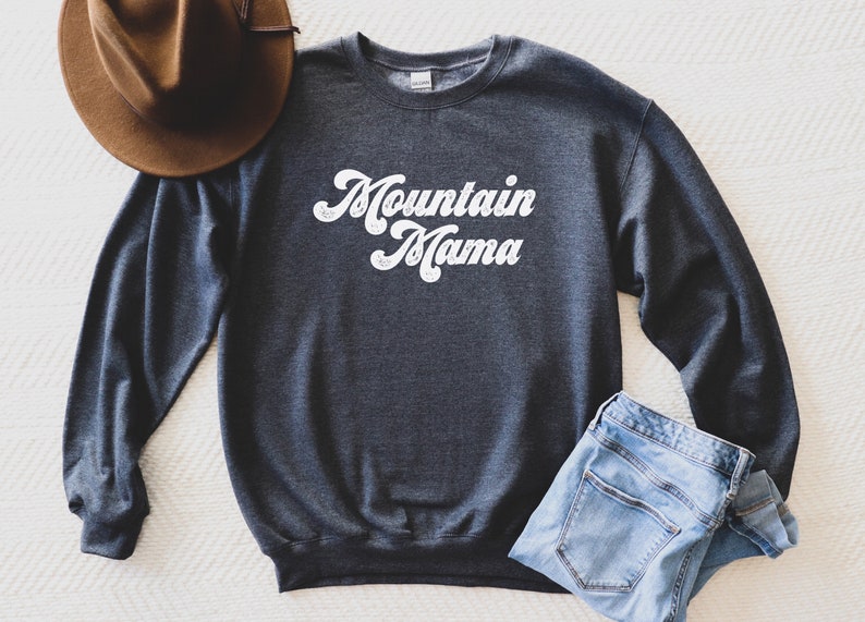 May include: A dark grey sweatshirt with the text "Mountain Mama" in white retro-style lettering.