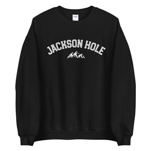 Peut inclure: Sweat-shirt noir avec un texte blanc qui dit "JACKSON HOLE" et un graphique de montagne blanc.