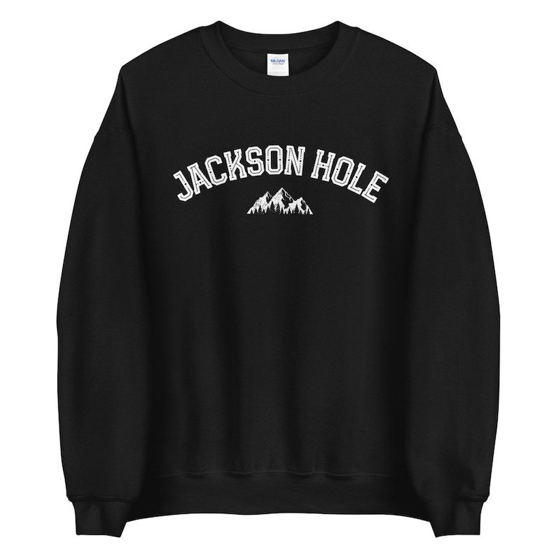 Peut inclure: Sweat-shirt noir avec un texte blanc qui dit "JACKSON HOLE" et un graphique de montagne blanc.
