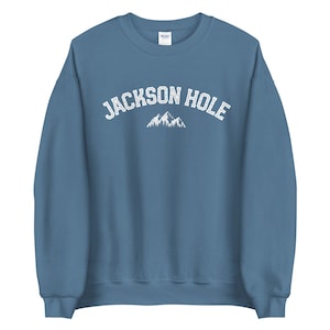 Peut inclure: Un sweat-shirt bleu avec le texte "JACKSON HOLE" en blanc et un graphique de montagne blanc.