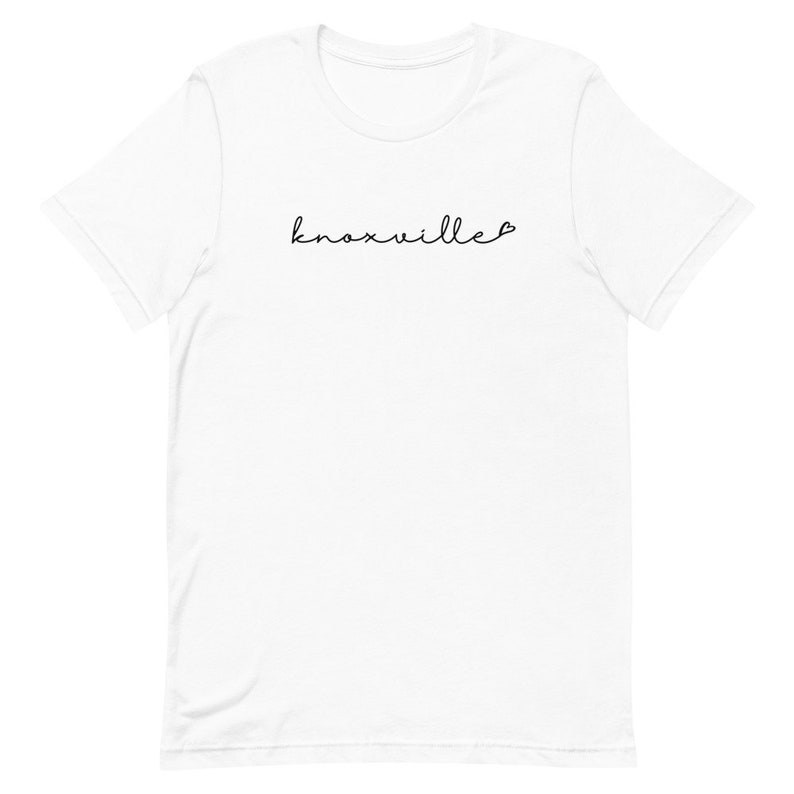 May include: White t-shirt with the word "Knoxville" in a handwritten font, with a small heart symbol at the end. The shirt has a crew neck and short sleeves.