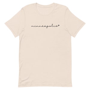 May include: A beige t-shirt with the word "minneapolis" written in black cursive script.