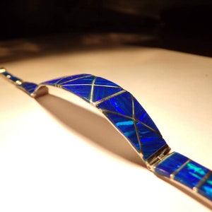 May include: A silver bracelet with a blue opal inlay. The opal is cut into geometric shapes and set in a silver band.