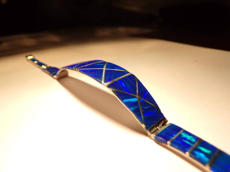 May include: A silver bracelet with a blue opal inlay. The opal is cut into geometric shapes and set in a silver band.