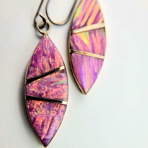 May include: A pair of dangle earrings with pink and iridescent opal-like stones set in silver. The stones are cut into a teardrop shape and have a gold-toned wire design.