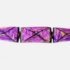 Pode incluir: Uma vista de perto de uma pulseira roxa com um design geom&eacute;trico. A pulseira &eacute; composta por tr&ecirc;s segmentos retangulares ligados por dobradi&ccedil;as. Cada segmento apresenta uma cor roxa vibrante e iridescente com detalhes em preto, criando um efeito visual marcante. A pulseira est&aacute; sobre um fundo branco.