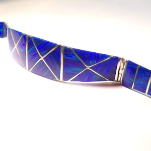 May include: A blue and silver bracelet with a geometric design. The bracelet is made of inlaid opal and silver.