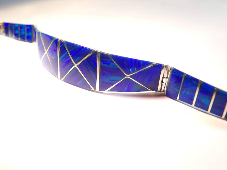 May include: A blue and silver bracelet with a geometric design. The bracelet is made of inlaid opal and silver.