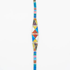 May include: A silver bracelet with colorful geometric designs. The bracelet features rectangular and triangular segments in shades of blue, pink, yellow, and green. The bracelet is displayed against a white background.