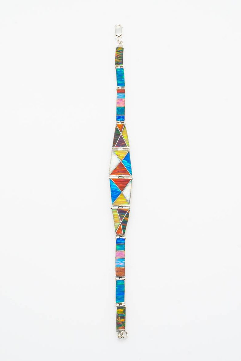 May include: A silver bracelet with colorful geometric designs. The bracelet features rectangular and triangular segments in shades of blue, pink, yellow, and green. The bracelet is displayed against a white background.