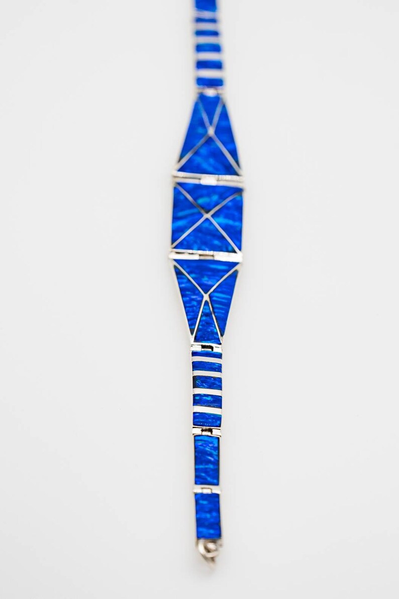 May include: A blue and silver bracelet with a geometric design. The bracelet is made of small, rectangular pieces of blue stone set in silver.