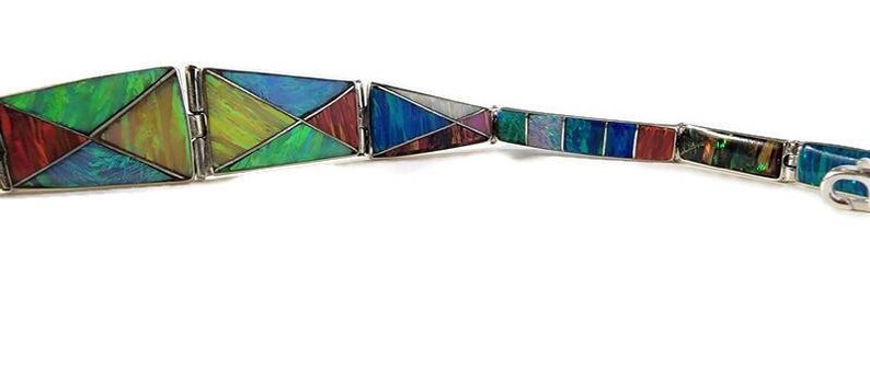May include: A multi-colored bracelet with geometric shapes made of opal and other gemstones. The bracelet is made of silver and has a clasp.