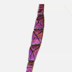 Pode incluir: Uma pulseira roxa com elos geom&eacute;tricos triangulares. Os elos s&atilde;o de um roxo vibrante com destaques iridescentes, conectados por metal prateado. A pulseira &eacute; exibida em um fundo branco.