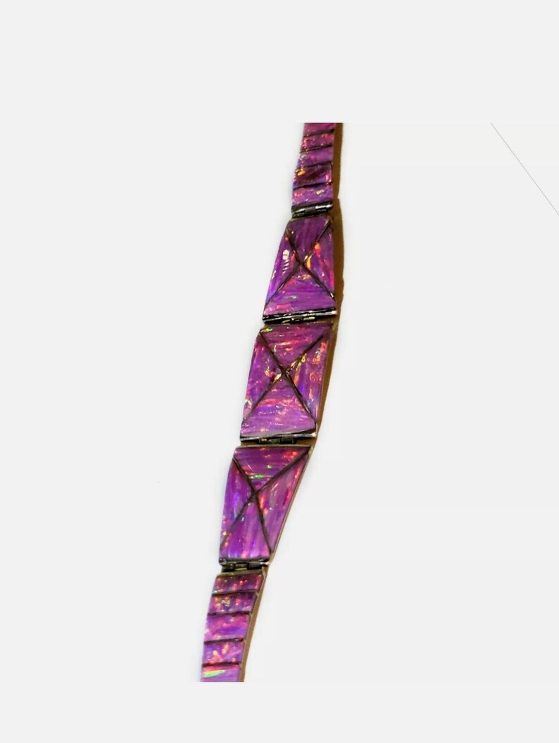 Pode incluir: Uma pulseira roxa com elos geom&eacute;tricos triangulares. Os elos s&atilde;o de um roxo vibrante com destaques iridescentes, conectados por metal prateado. A pulseira &eacute; exibida em um fundo branco.